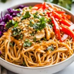 Bowl Of Spicy Peanut Soba Noodle Salad Garnished With Crushed Peanuts And Fresh Herbs On A Neutral Background