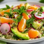 Spicy Radish Quinoa Salad In A White Plate Topped With Avocado And Tangerines, Garnished With Mint Leaves