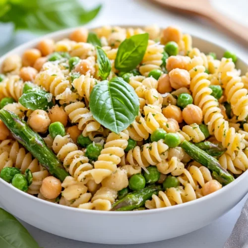 Fresh Spring Pasta Salad In A White Bowl With Asparagus, Peas, And Lemon Vinaigrette, Garnished With Basil And Pine Nuts