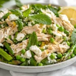 Spring Salad With Chicken And Lemon Dressing Served On A White Plate, Topped With Feta, Mint Leaves, And Lemon Slices