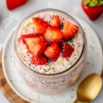 Close-Up Of Strawberries And Cream Overnight Oats In A Glass Jar, Topped With Fresh Strawberries And Chia Seeds