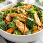 Bowl Of Thai Peanut Chicken Stir-Fry With Broccoli And Carrots, Garnished With Sesame Seeds And Cilantro