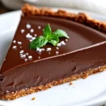 Vegan Chocolate Pie Topped With Sea Salt And Mint Leaves, Served On A White Plate With A Golden Crust