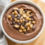 Bowl Of Vegan Protein Fluff Topped With Dark Chocolate Chips And Peanuts On A Light Wooden Table