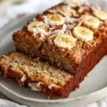 Sliced Apple Banana Bread On A White Plate, Topped With Caramelized Coconut And Garnished With Banana Slices