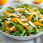 Fresh Arugula Salad With Lemon Dressing, Topped With Shaved Vegetables And Almonds In A White Bowl, Garnished With Parmesan.