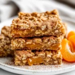 Stack Of Baked Oatmeal Apricot Bars On A White Plate Garnished With Fresh Apricot Slices