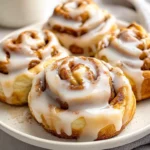 Fluffy Banana Bread Cinnamon Rolls Drizzled With Cream Cheese Icing On A White Plate, Sprinkled With Cinnamon