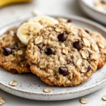 Platter Of Chewy Banana Oat Cookies With Melted Chocolate Chips And A Banana Slice Garnish On A White Plate.