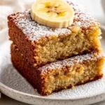 Slices Of Best Banana Bread Cake Dusted With Icing Sugar On A White Plate, Garnished With Banana Slices