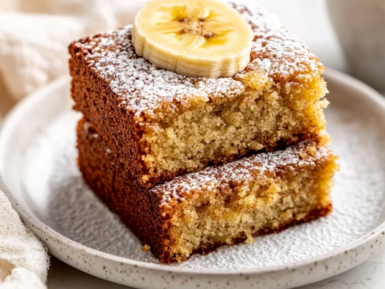 Best Banana Bread Cake Recipe: Moist, Easy &Amp; Healthy Dessert 2 Slices Of Best Banana Bread Cake Dusted With Icing Sugar On A White Plate, Garnished With Banana Slices