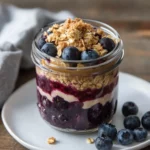 Blueberry Cobbler Overnight Oats In A Mason Jar Topped With Crumble And Fresh Blueberries, Served On A White Plate