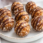 Close-Up Of Caramel Energy Balls On A White Plate, Topped With Toasted Coconut And Chocolate Drizzle.