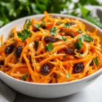 Colorful Carrot Raisin Salad In A White Bowl, Garnished With Fresh Parsley And Creamy Dressing