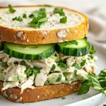 Close-Up Of A Chicken Salad Sandwich With Green Mayo, Avocado, And Microgreens On A White Plate.