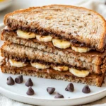 Chocolate Banana Sandwich On A White Plate, Showcasing Layers Of Peanut Butter, Banana, And Chocolate Chips