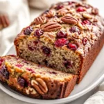 Sliced Cranberry Banana Bread On A White Plate With Chopped Pecans, Showcasing A Moist Texture And Cranberries
