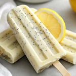 Creamy Lemon Poppy Seed Ice Pops In A Clear Cup Garnished With A Lemon Slice And Poppy Seeds On A Gray Background.