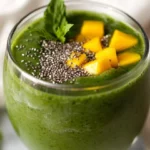 Creamy Spirulina Green Smoothie With Mango In A Clear Glass Garnished With Hemp Seeds And Mint Leaves