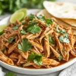 Crockpot Cilantro Lime Chicken On A White Plate, Garnished With Cilantro And Served With Warm Tortillas
