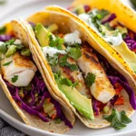 Plate Of Easy Fish Tacos Filled With Fish, Red Cabbage, And Avocado, Drizzled With Sauce And Garnished With Cilantro