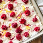 Frozen Yogurt Bark With Raspberries On A White Parchment-Lined Baking Sheet, Topped With Lemon Zest.