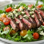 Gorgonzola Steak Salad On A White Plate Topped With Grilled Steak, Gorgonzola Cheese, And Cherry Tomatoes