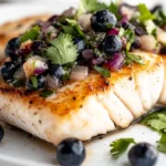 Grilled Halibut With Blueberry Salsa On A White Plate, Garnished With Cilantro And Vibrant Blueberries