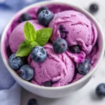 Bowl Of Homemade Blueberry Frozen Yogurt Topped With Fresh Blueberries And Mint, On A Simple White Background