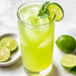Refreshing Homemade Limeade Without Refined Sugar In A Glass With Ice, Garnished With Lime Slice And Mint On A Marble Countertop