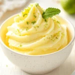 How To Make A Pineapple Whip Served In A White Bowl, Garnished With Lime Zest And Mint Leaves.