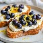 Lemon Blueberry Toast Topped With Ricotta, Fresh Blueberries, And Lemon Zest On A White Plate