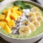 Lime Coconut Smoothie Bowl Topped With Banana, Mango, Pineapple, And Shredded Coconut On A White Plate
