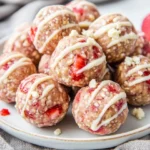 Plate Of No-Bake Strawberry Protein Balls Drizzled With White Chocolate And Topped With Crushed Strawberries