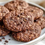 Plate Of No Sugar Chocolate Oatmeal Cookies Topped With Cacao Nibs On A White Plate, Set On A Soft Beige Cloth.