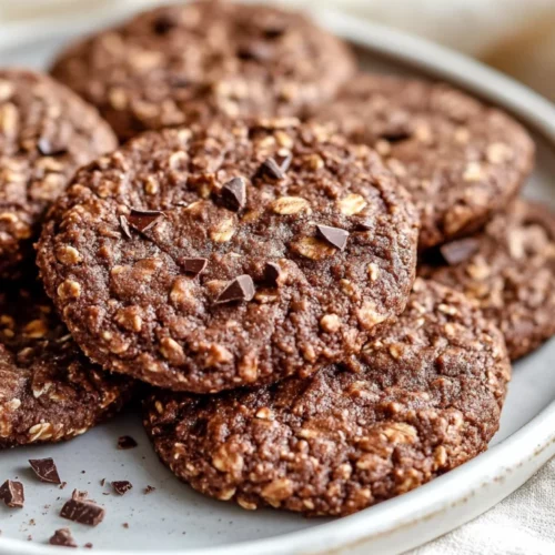 Plate Of No Sugar Chocolate Oatmeal Cookies Topped With Cacao Nibs On A White Plate, Set On A Soft Beige Cloth.