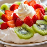 Pavlova Dessert Topped With Fresh Strawberries And Kiwis On A White Plate With Whipped Cream