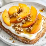 Peach Toast Breakfast On A White Plate Topped With Yogurt, Peach Slices, And Walnuts, Drizzled With Honey.