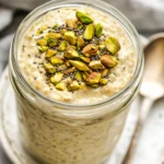 Jar Of Pistachio Overnight Oats Topped With Pistachio Butter And Chopped Nuts On A White Plate