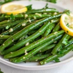 Sautéed Green Beans On A White Plate, Garnished With Lemon Zest And Parsley, Served With A Lemon Slice.