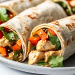 Sesame Chicken Wraps On A White Plate, Filled With Colorful Veggies And Chicken, Garnished With Sesame Seeds And Cilantro