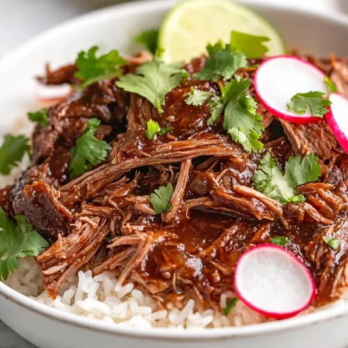 Savory Slow Cooker Barbacoa Beef - Perfect For Tacos Or Bowls 2 Bowl Of Slow Cooker Barbacoa Beef Over Rice, Garnished With Cilantro And Lime Wedges, On A Wooden Table.