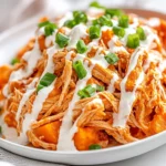 Plate Of Slow Cooker Buffalo Chicken Over Baked Sweet Potatoes, Drizzled With Ranch Dressing And Garnished With Green Onions