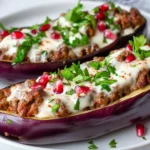 Stuffed Eggplant Boats With Ground Beef And Yogurt Sauce, Garnished With Parsley And Pomegranate Seeds On A White Plate