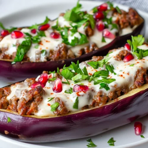 Stuffed Eggplant Boats With Ground Beef And Yogurt Sauce, Garnished With Parsley And Pomegranate Seeds On A White Plate