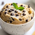 Bowl Of Vegan Edible Cookie Dough Garnished With Chocolate Chips And Mint Leaves On A Neutral Background