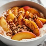 Warm Peach Yogurt Bowl With Caramelized Peaches And Granola In A White Bowl On A Neutral Surface